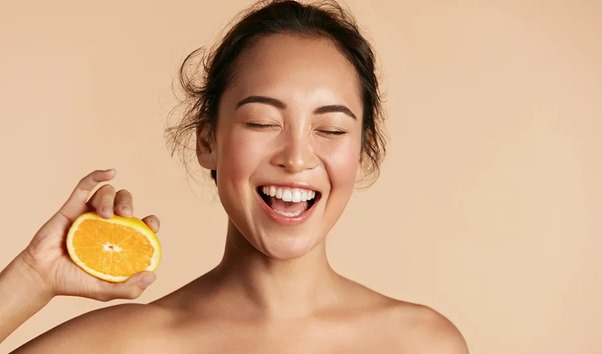 Image of a woman with clear skin holding an orange.